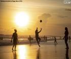 Strand bij zonsondergangtijd, met mensen die sporten op de kust, surfers en anderen op het water doen